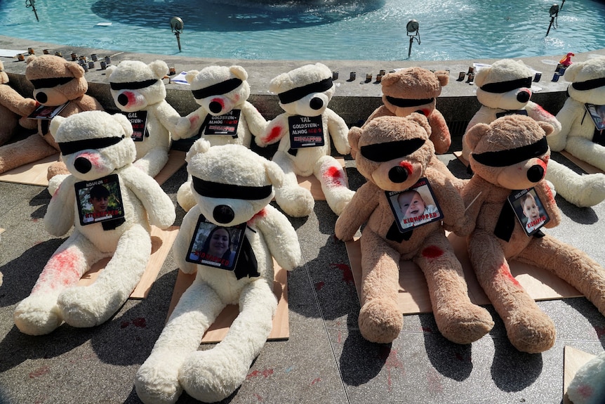 Teddy bears laid out in front of a fountain with a picture of a child hanging from the neck of each