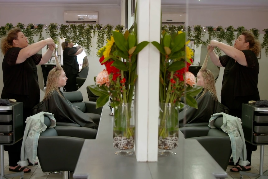 A woman cuts the hair of another woman in a salon.