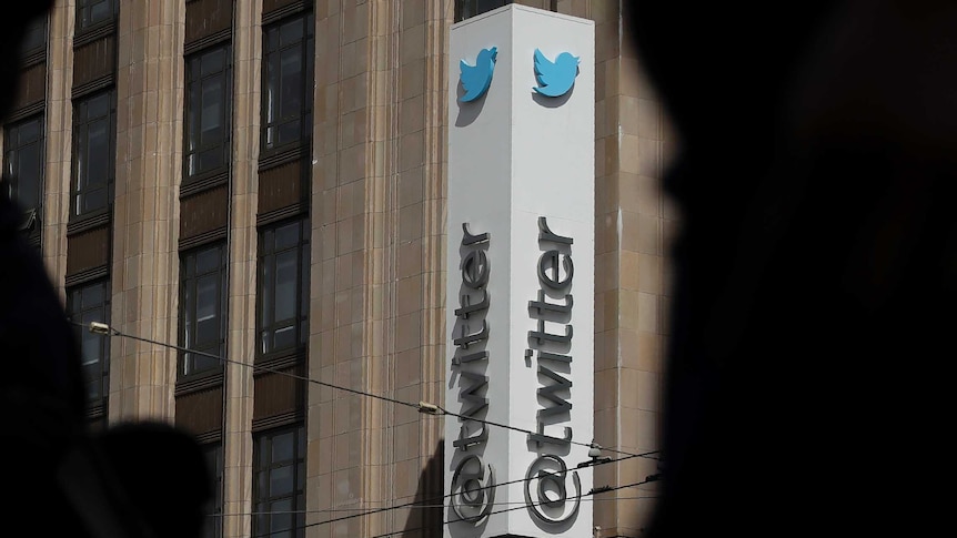 Shadows of people in the foreground, with the Twitter logo on the side of a building