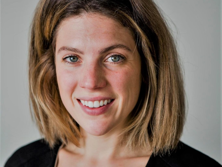 A woman smiles at the camera in front of a grey background.