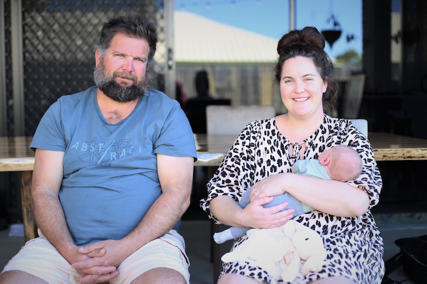 Two people sit outside holding their baby