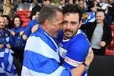 A Greek rugby league player tears up as he stands with his arm around a man wearing a Greek flag.