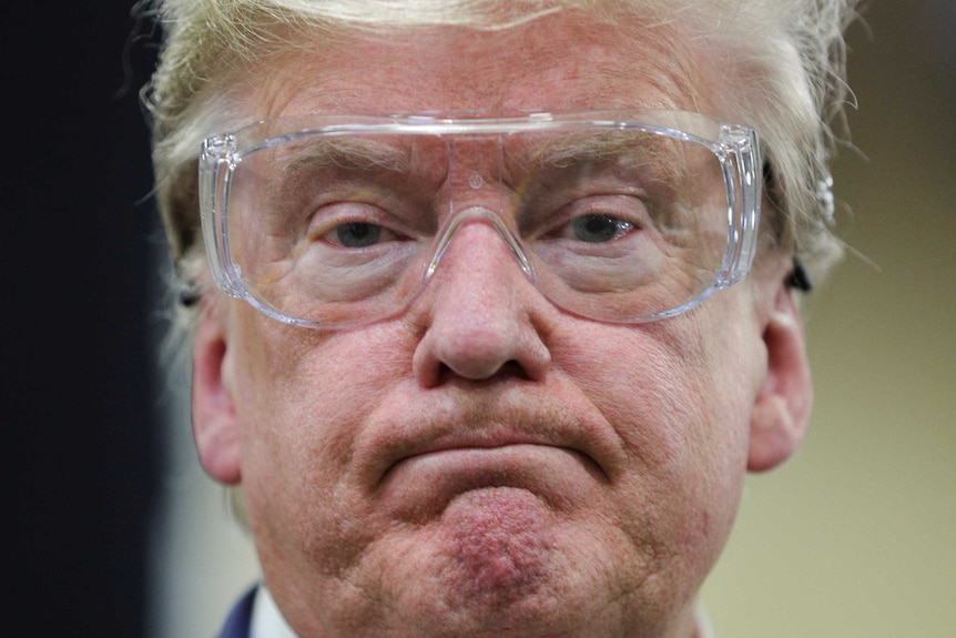 US President Donald Trump watches workers on the assembly line while wearing goggles