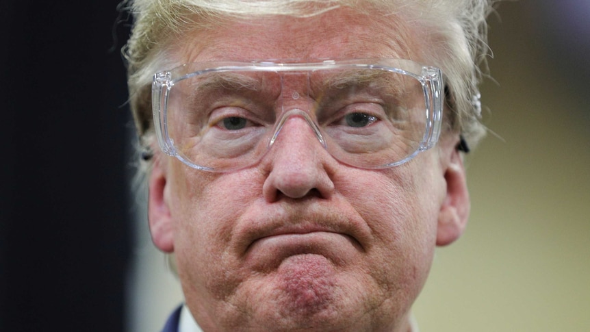 US President Donald Trump watches workers on the assembly line while wearing goggles