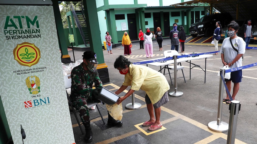 Residents practice social distancing as they queue up for free rice from a rice dispenser machine.