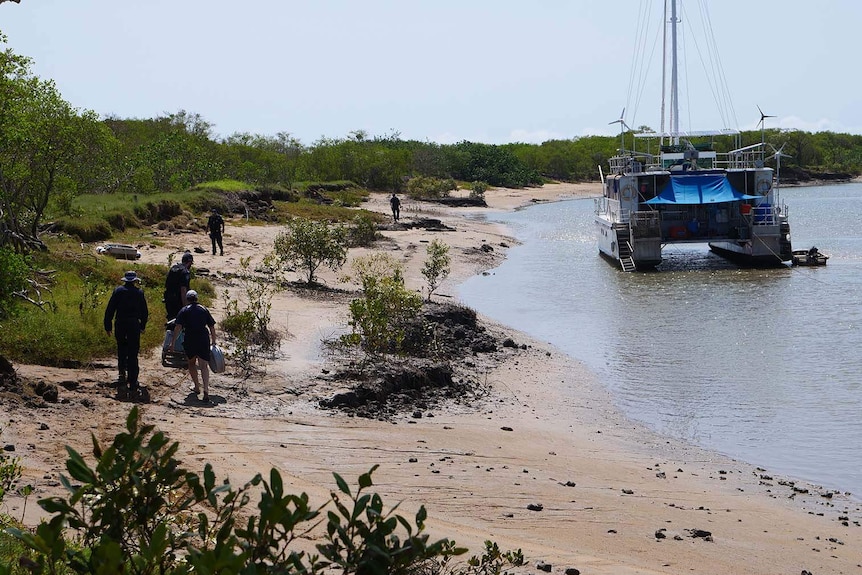 Police officers searching a riverbank near a moored catamaran