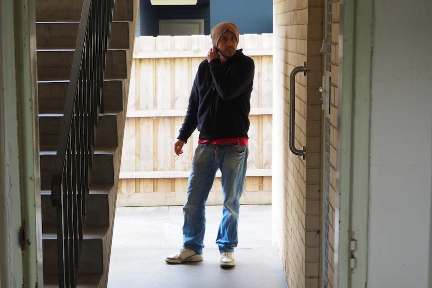 Joel Sinclair outside in a doorway near stairs, touching his hat.