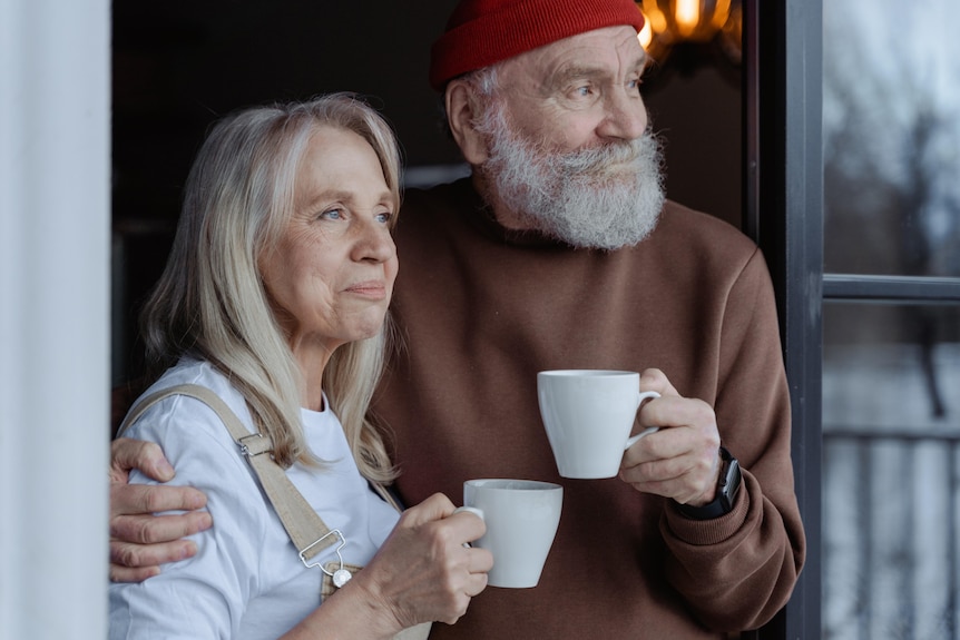 A woman and a man with a grey beard and beanie share a cup or tea or coffee.