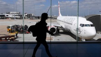 The photo shows the silhouette of a woman walking inside Melbourne Airport as a plane prepares for boarding.