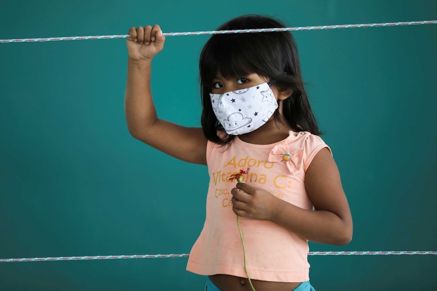 A little Brazilian girl in a face mask holding a flower