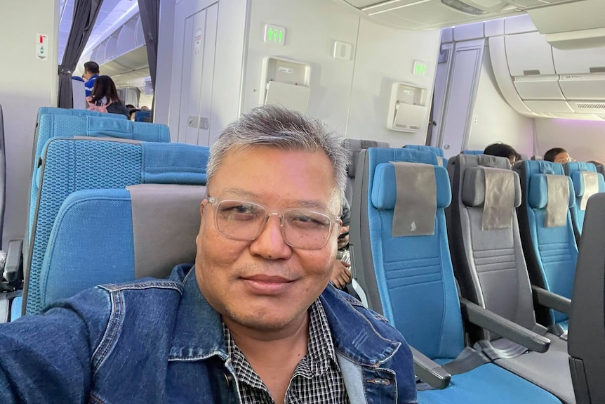 Selfie of a Burmese man with silver hair and glasses sitting on a plane.