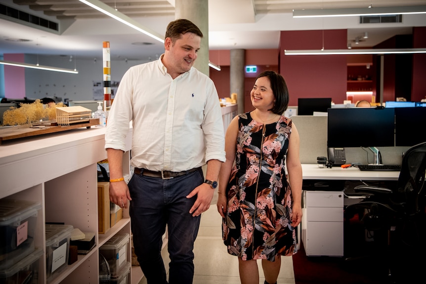A man walking together with a woman in an office environment. 