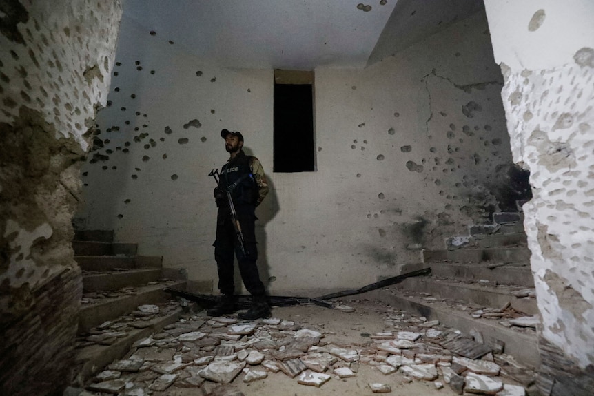 Picture of a policeman inside a damaged building with bullet holes 