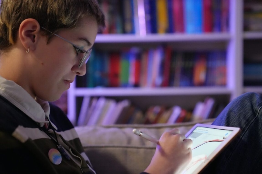 A teenage boy wearing glasses is shown side on, very focused while drawing on an ipad with an apple pen. 