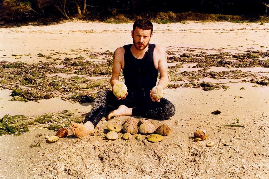 A young man with a collection of urchins on a beach.