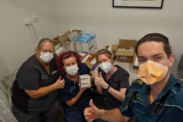 Two nurses, a doctor in scrubs and an ambulance officer standing in front of medical supplies