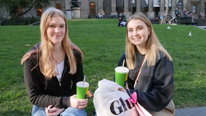 Students Lulu Collins and Erin Anderson holding Boost juice containers in front of a grassy park in Melbourne.