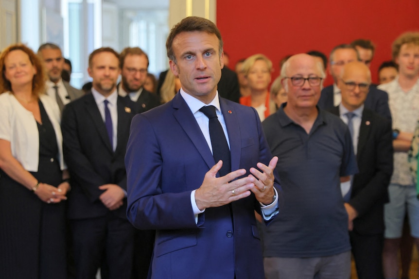 A man in a blue suit speaks to a room full of people 