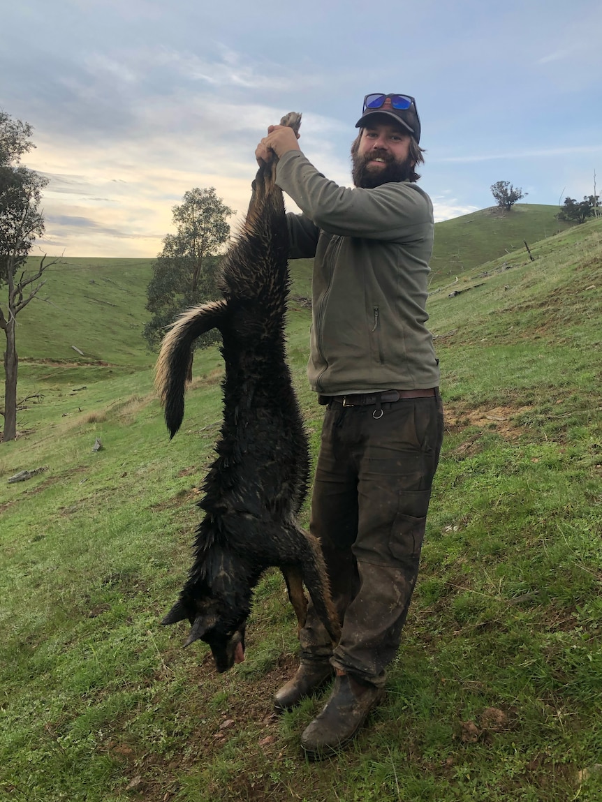 A man holds up a dead animal, dog-like in appearance, by its hind legs.