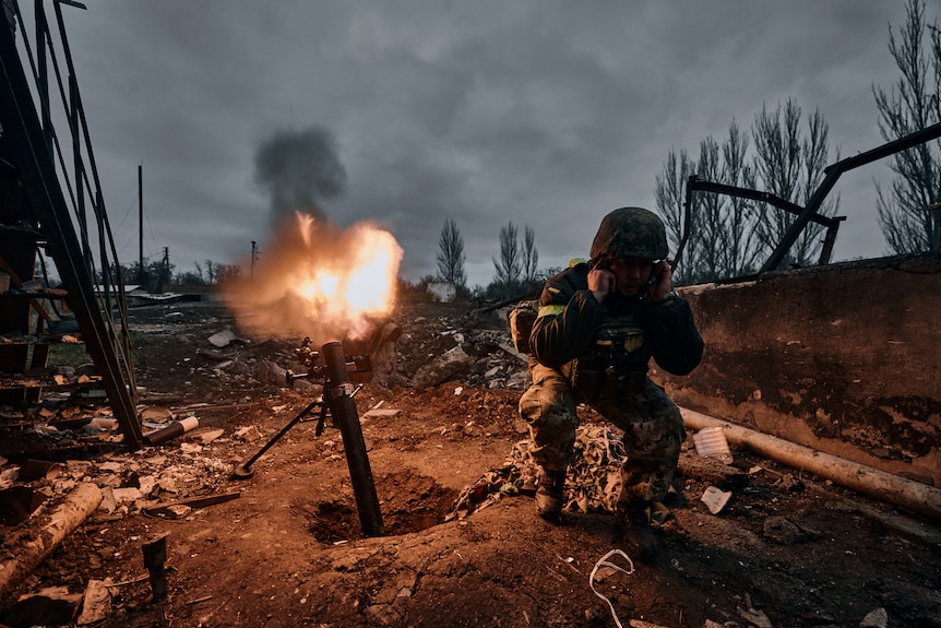 A Ukrainian soldier puts his fingers in his ears as he fires a mortar at Russian positions in Bakhmut.