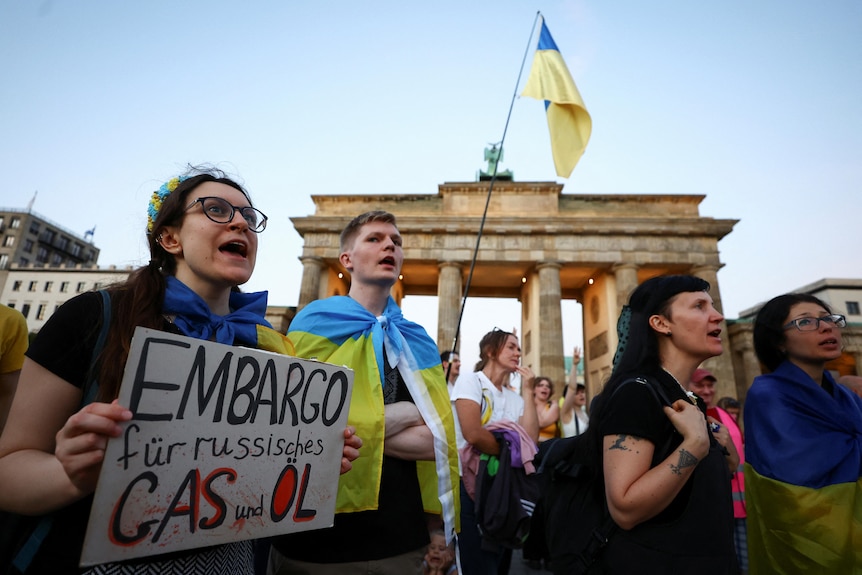 Los manifestantes sostienen carteles y ondean banderas amarillas y azules frente a la Puerta de Brandenburgo.