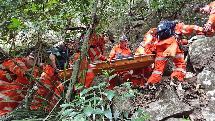 Emergency Crew dressed in orange carry out a person on an orange stretcher through rugged terrain
