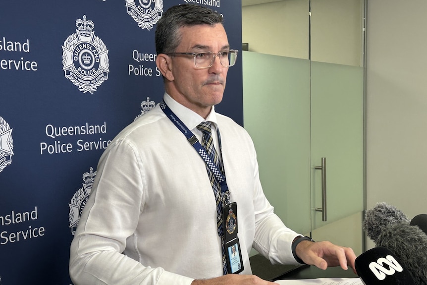 A bespectacled man with short, dark hair, wearing a police lanyard, speaks to the media.