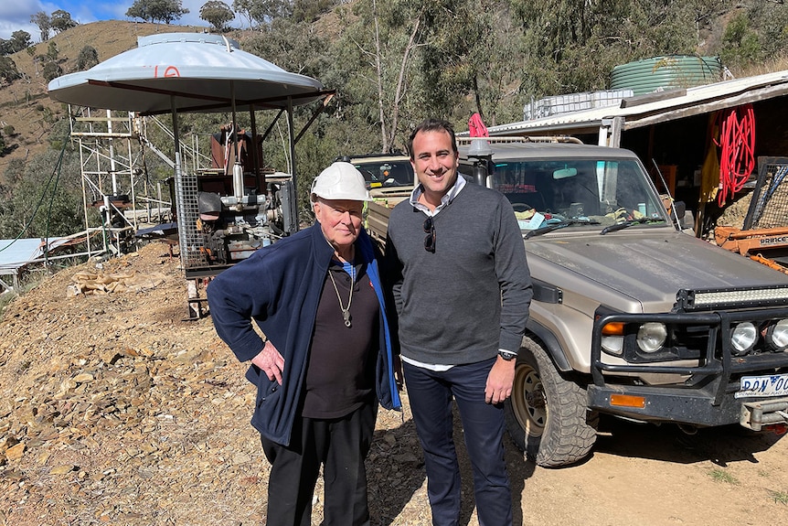 Two men stand in front of a ute with a series of small gold processing machinery in the background.