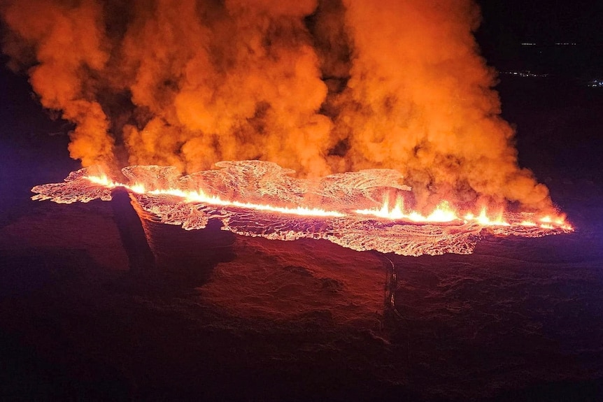 Orange smoke billows from boiling hot lava seen from above, lighting up the dark surroundings.