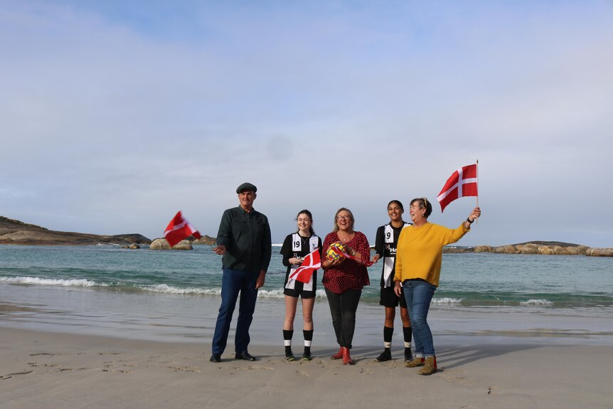 Five people wave Denmark flag on beach