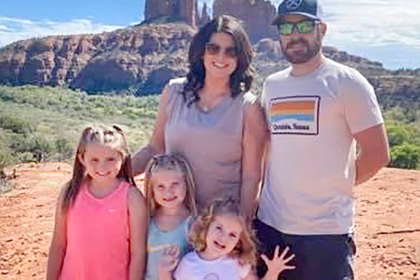 Two parents and three young daughters pose for a photo while standing in the desert.