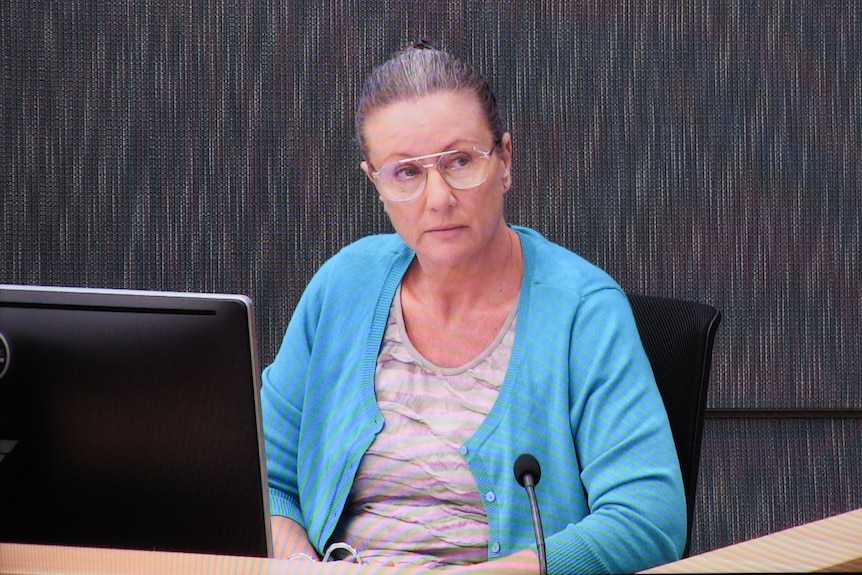 Woman with hair in bun and blue cardigan wearing glasses sitting down