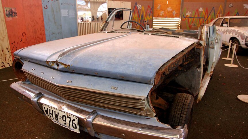 A 1963 blue EH holden with its roof cut off and side panel near the tyre missing.