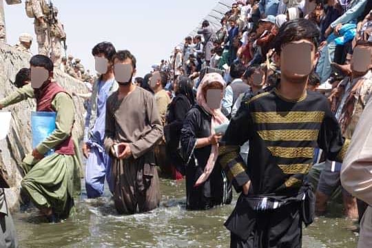 A crowd of Afghans stand on a sewage-filled trench at Kabul airport, their faces have been blurred