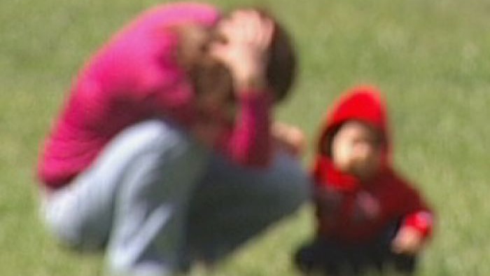 a blurred image of woman kneeling in a field with he hand on head and toddler holding on.