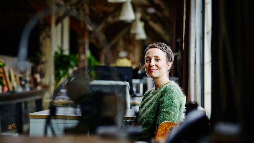 a woman smiles at the camera, sitting in a warehouse style work space