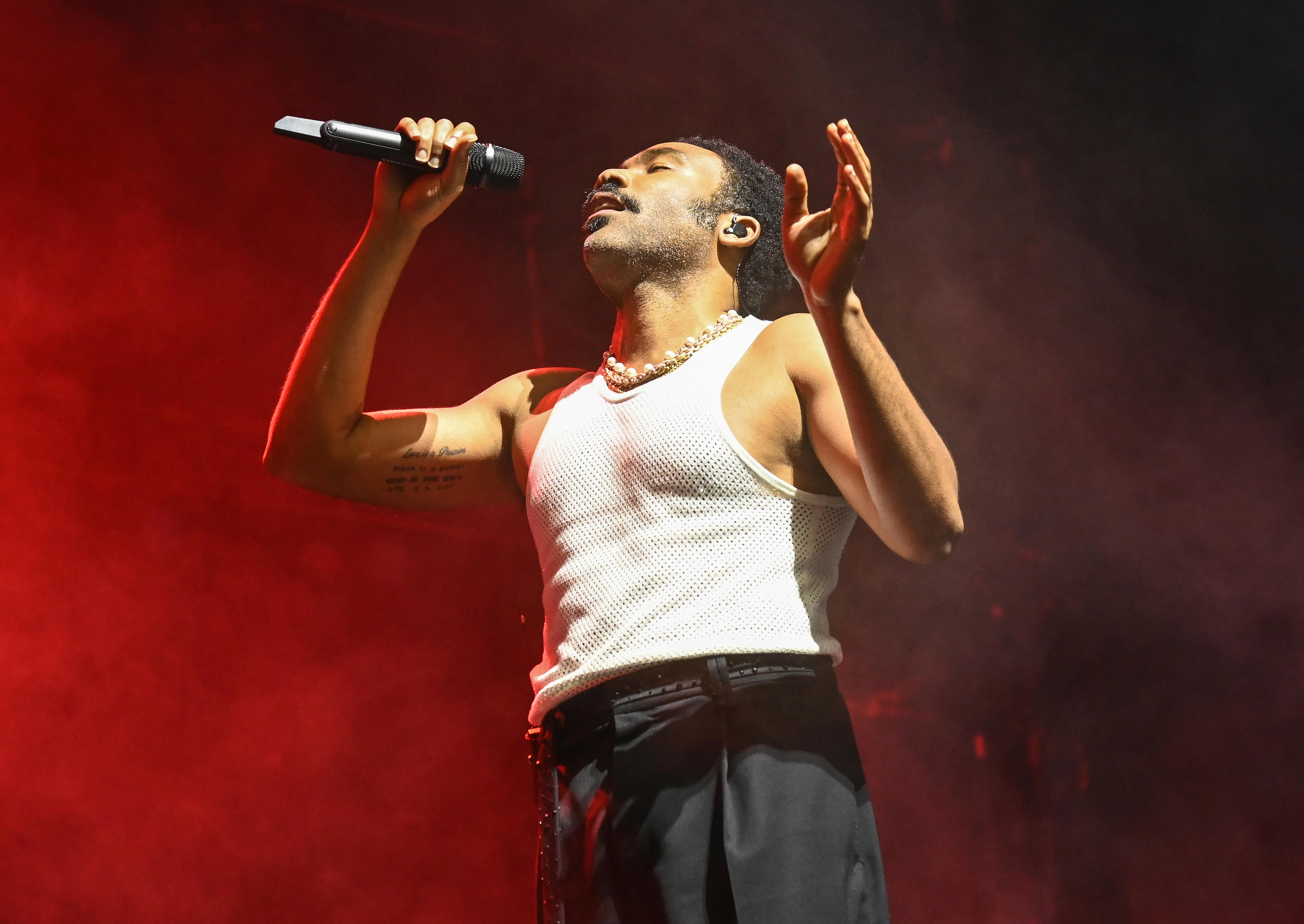 Donald Glover performs in a white singlet and dark trousers on a stage with red lighting
