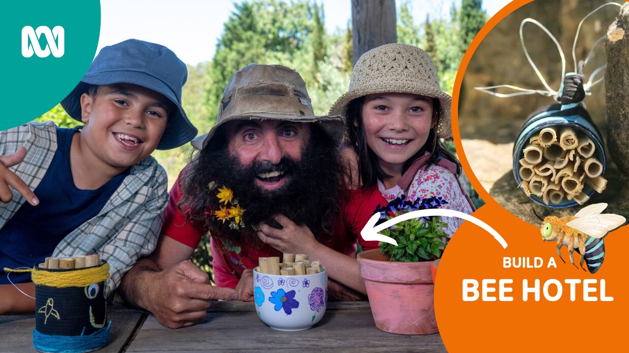 Children wearing hits smile excitedly beside a man with a bushy beard. Containers with bamboo sticks are in front of them