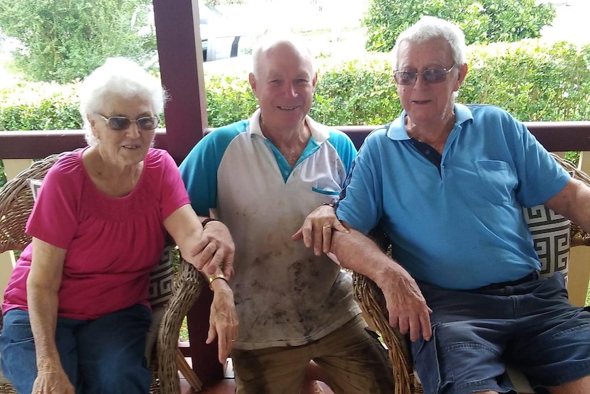 An elderly man and woman seated, with a man kneeling between them, all smiling.