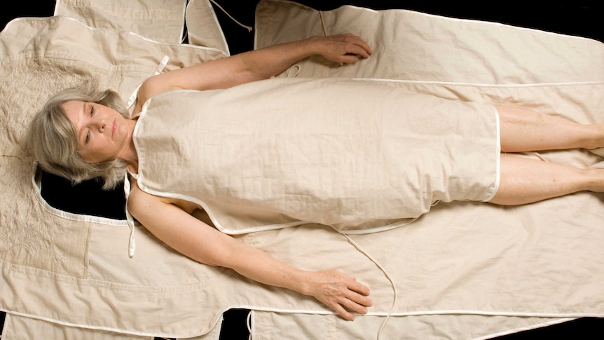 Caucasian woman lying on cotton fabric shapes, that form a burial shroud.