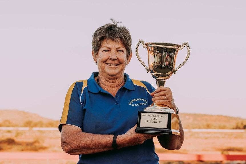A woman holding a trophy at bush races meeting. 