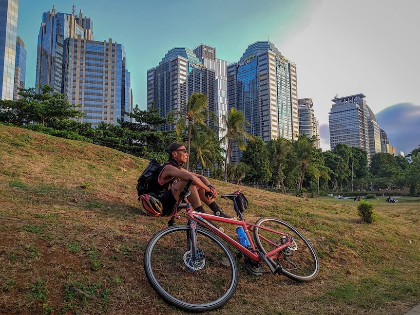 Adhito Harinugroho pictured sitting on a hill with his bike next to him, as the sun begins to set.