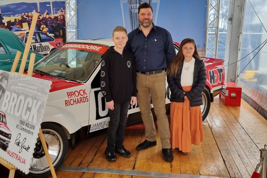 A man with his two children in front of a car.