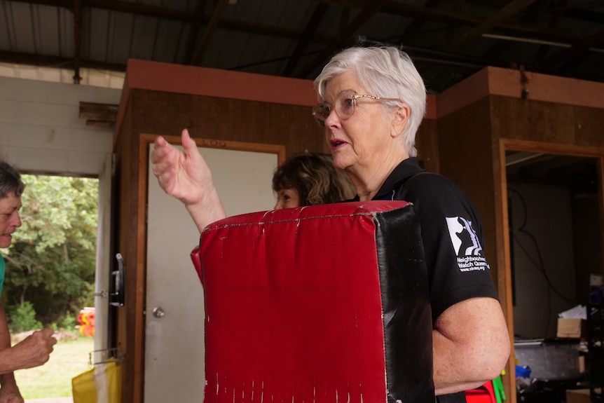 Older woman holds boxing pad 
