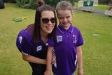 Katherine and Ella stand next to each other on an oval, wearing purple shirts. Katherine is bending down to Ella's height.