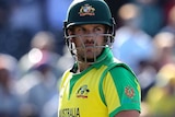 Carrying his gloves and bat, Aaron Finch looks back over his shoulder with a disappointed look on his face.