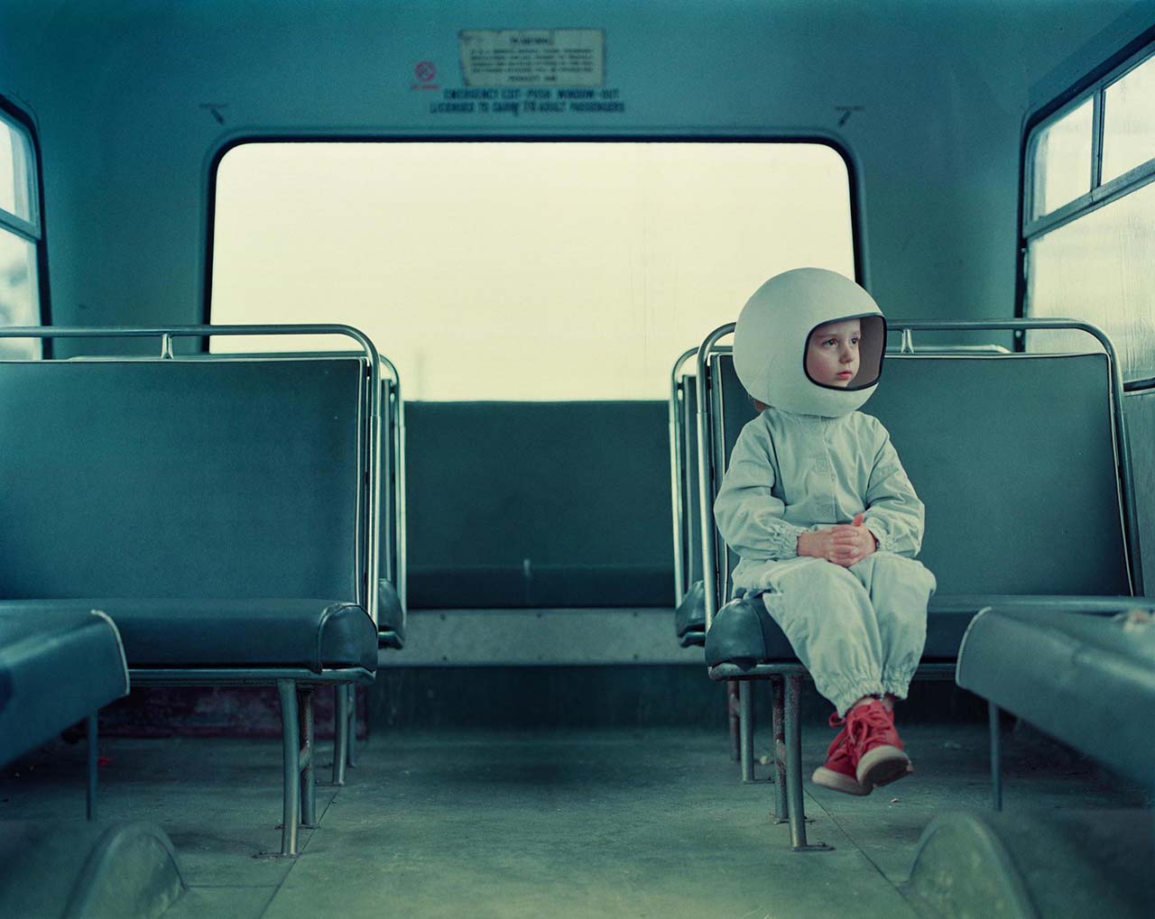 A young girl wearing a spacesuit costume and helmet sits on an empty bus.