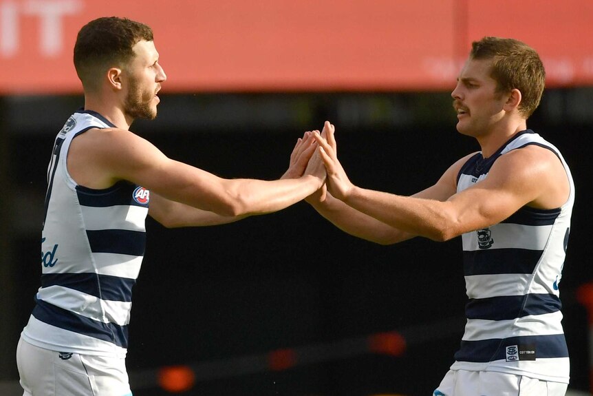 Two Geelong AFL players high five each other as they celebrate a goal against the Bombers.