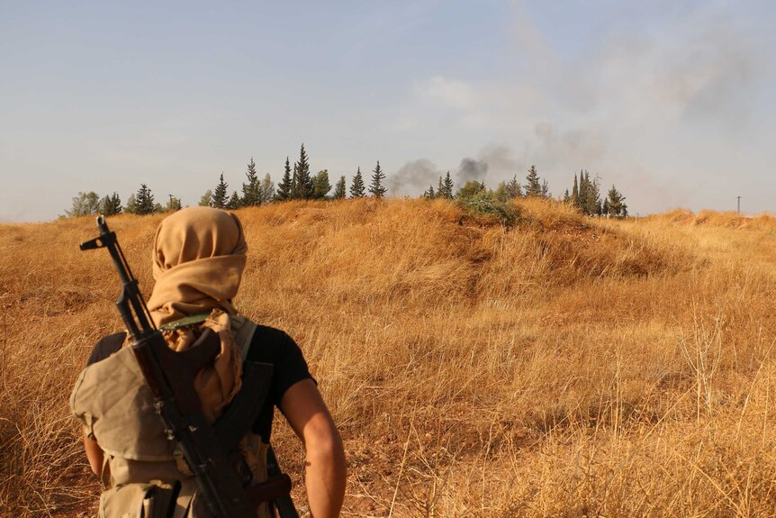 A rebel fighter looks at smoke billowing from south of the Syrian city of Aleppo