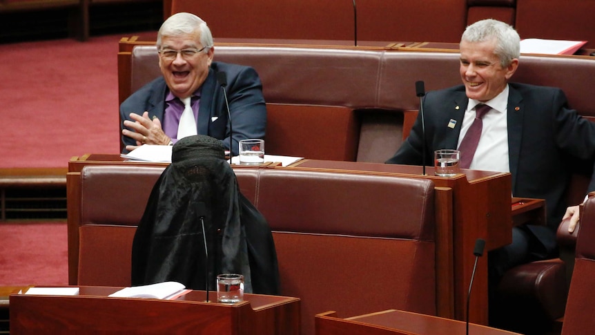 Pauline Hanson in burqa, Malcolm Roberts and Brian Burston laugh in background